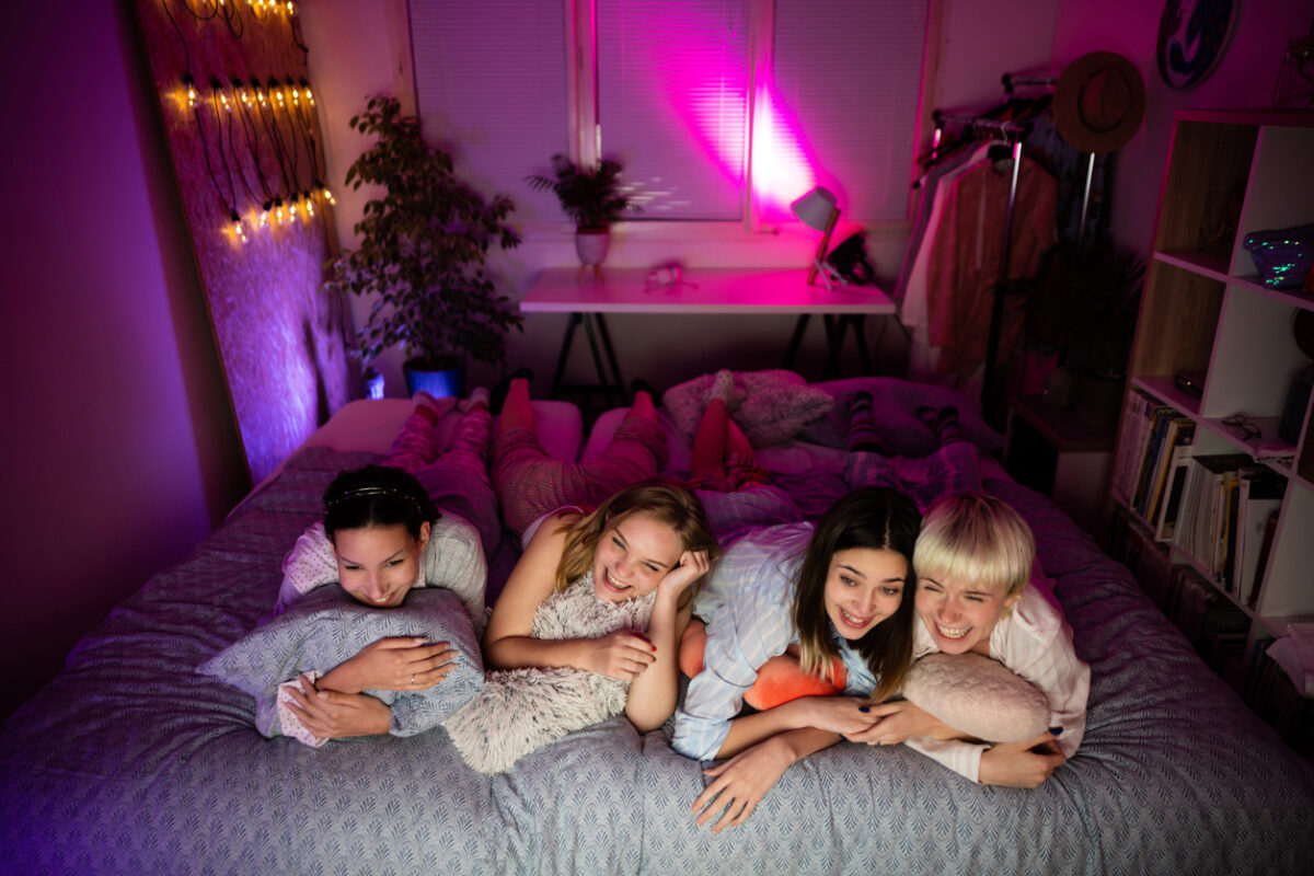 Quattro amiche sdraiate sul letto che guardano un film insieme
