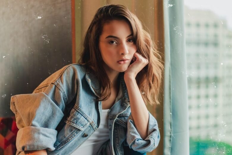 Una ragazza con una giacca di jeans appoggiata con il gomito alla finestra