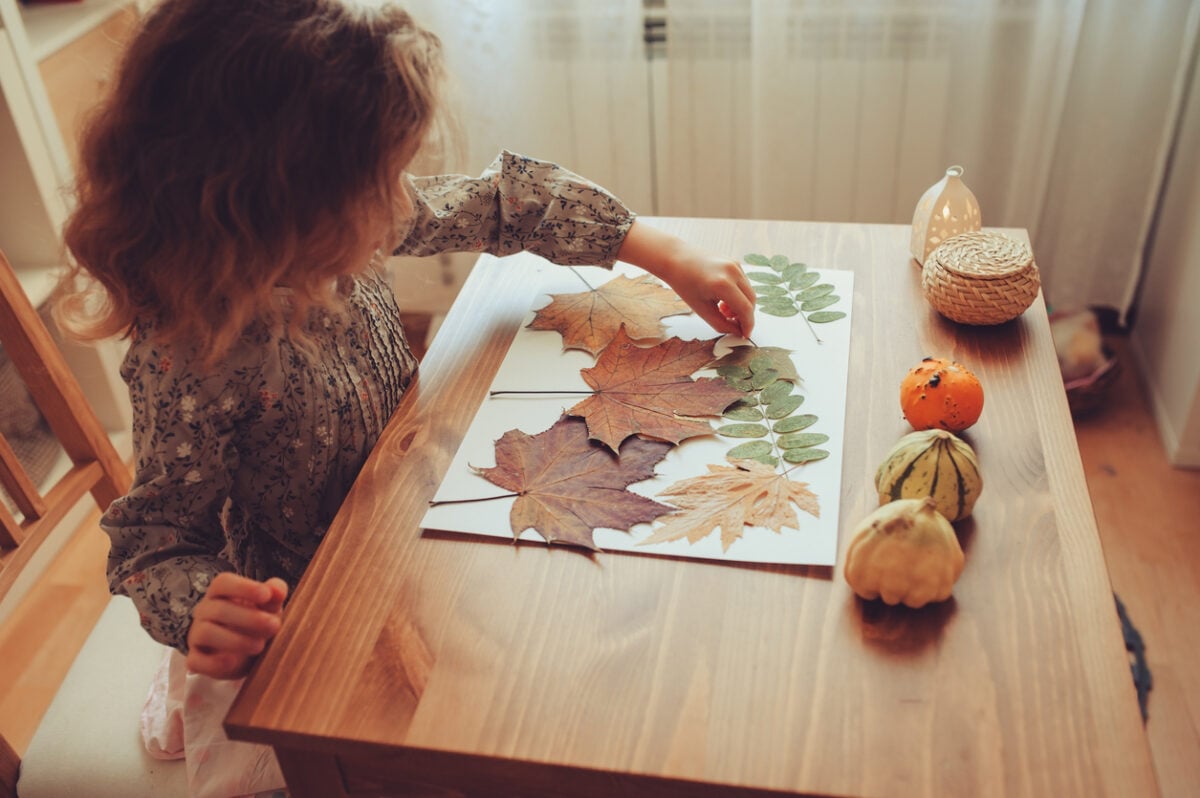 Una bambina sta facendo un disegno con le foglie autunnali