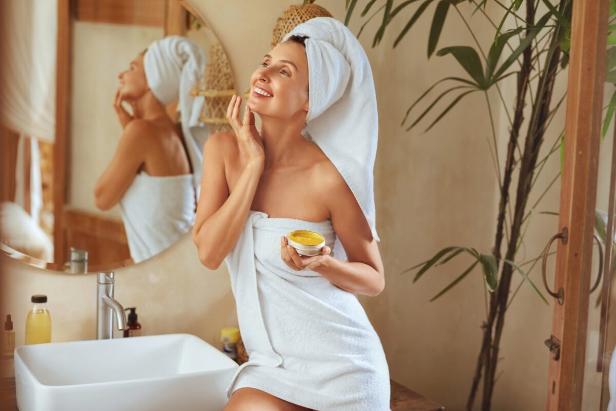 Donna si guarda allo specchio mentre si mette la crema sul viso