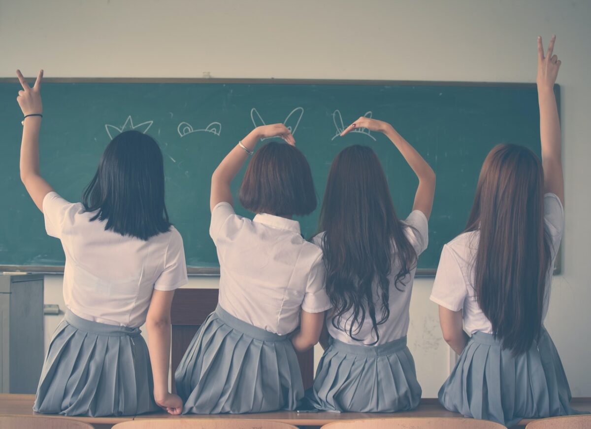 Ragazze in uniforme scolastica di spalle sedute sui banchi di scuola