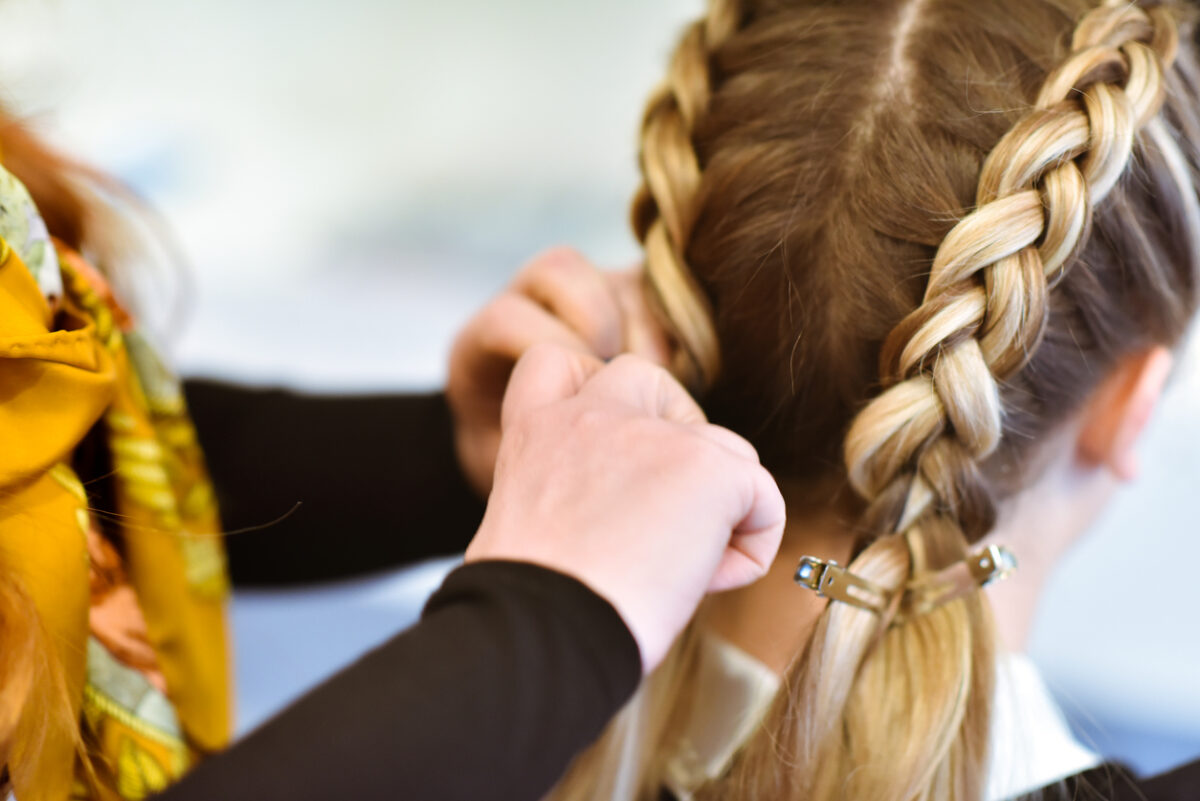 Una ragazza fa la treccia olandese a un'amica coi capelli buondi