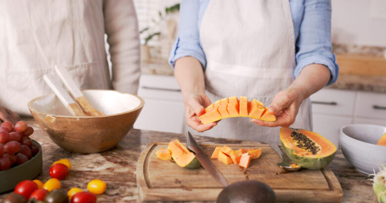 Donna in cucina sta tagliano a pezzi la papaya per usarla in qualche ingrediente