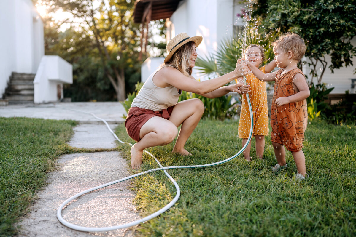 mamma che gioca con i bambini in giardino con il tubo dell'innaffiatoio