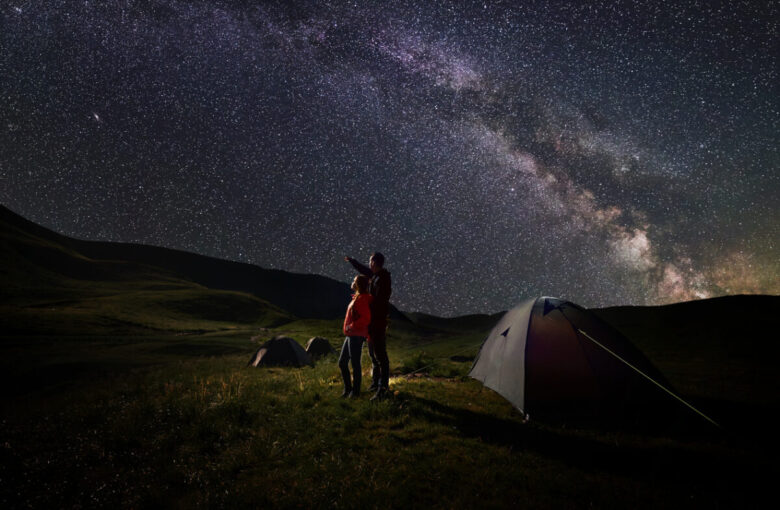 persone che stanno osservando un cielo di stelle durante una vacanza in tenda
