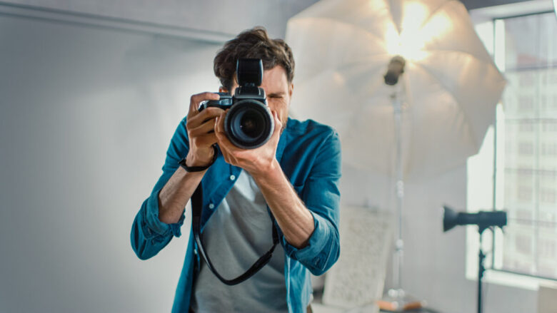 Nello studio fotografico con attrezzature professionali: ritratto del famoso fotografo che tiene una fotocamera all'avanguardia che scatta foto con Softbox lampeggianti in background