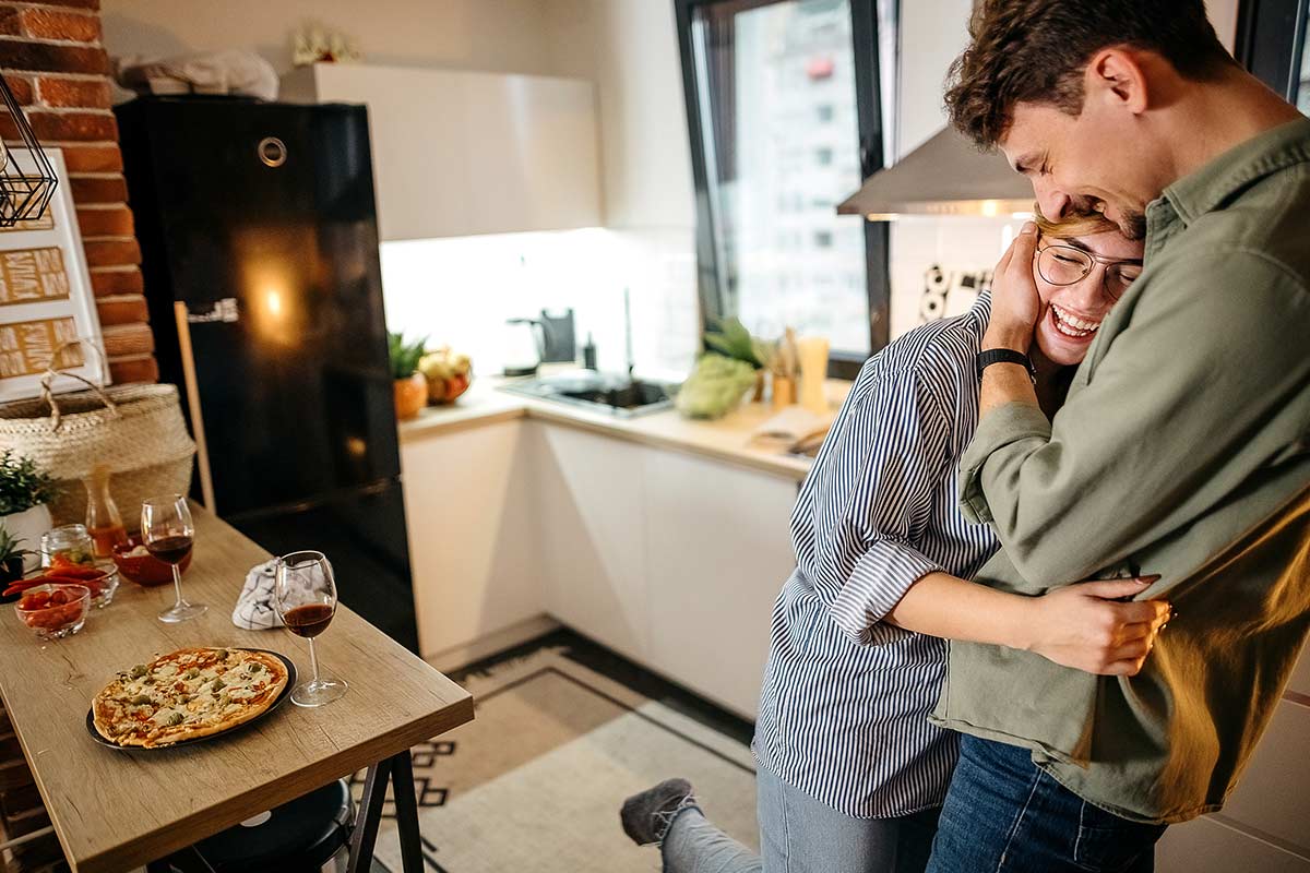 Uomo e donna sorridono abbracciati in cucina (iStock)