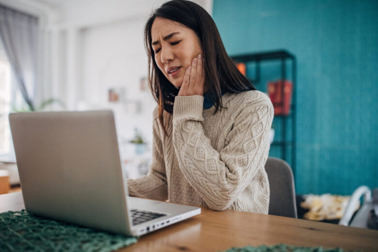 Ragazza con mal di denti, forse brusimmo, davanti al pc