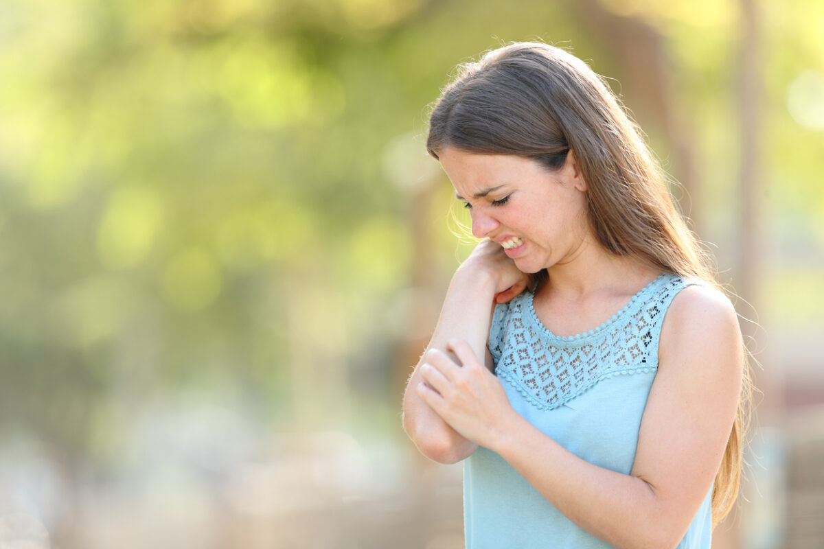 Woman scratching because her arm itches in a park