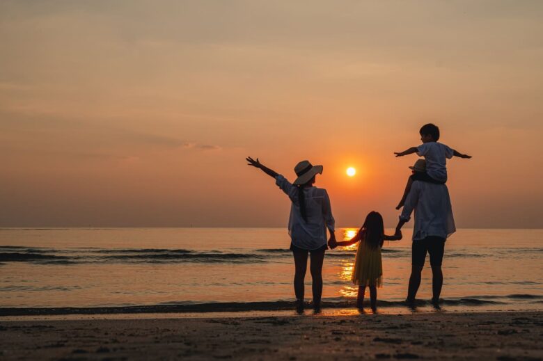 Famiglia felice insieme sulla spiaggia in vacanza. La famiglia si tiene per mano godendosi il tramonto sulla spiaggia.
